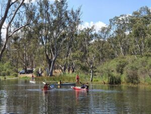 Children canoing and paddle boarding on a river with trees in the background